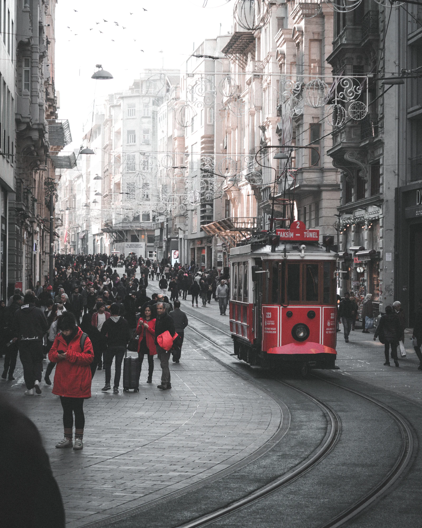 People walking along a shopping street next to a red tram