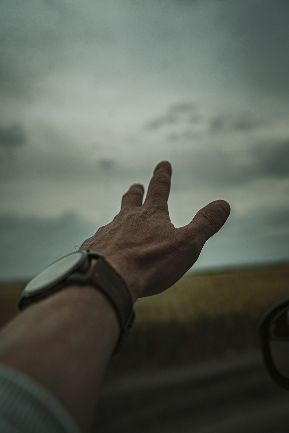 person wearing silver watch with white clouds in the background