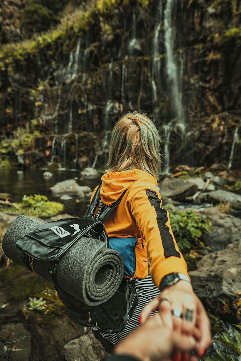 woman in yellow jacket and black pants sitting on rock near river during daytime