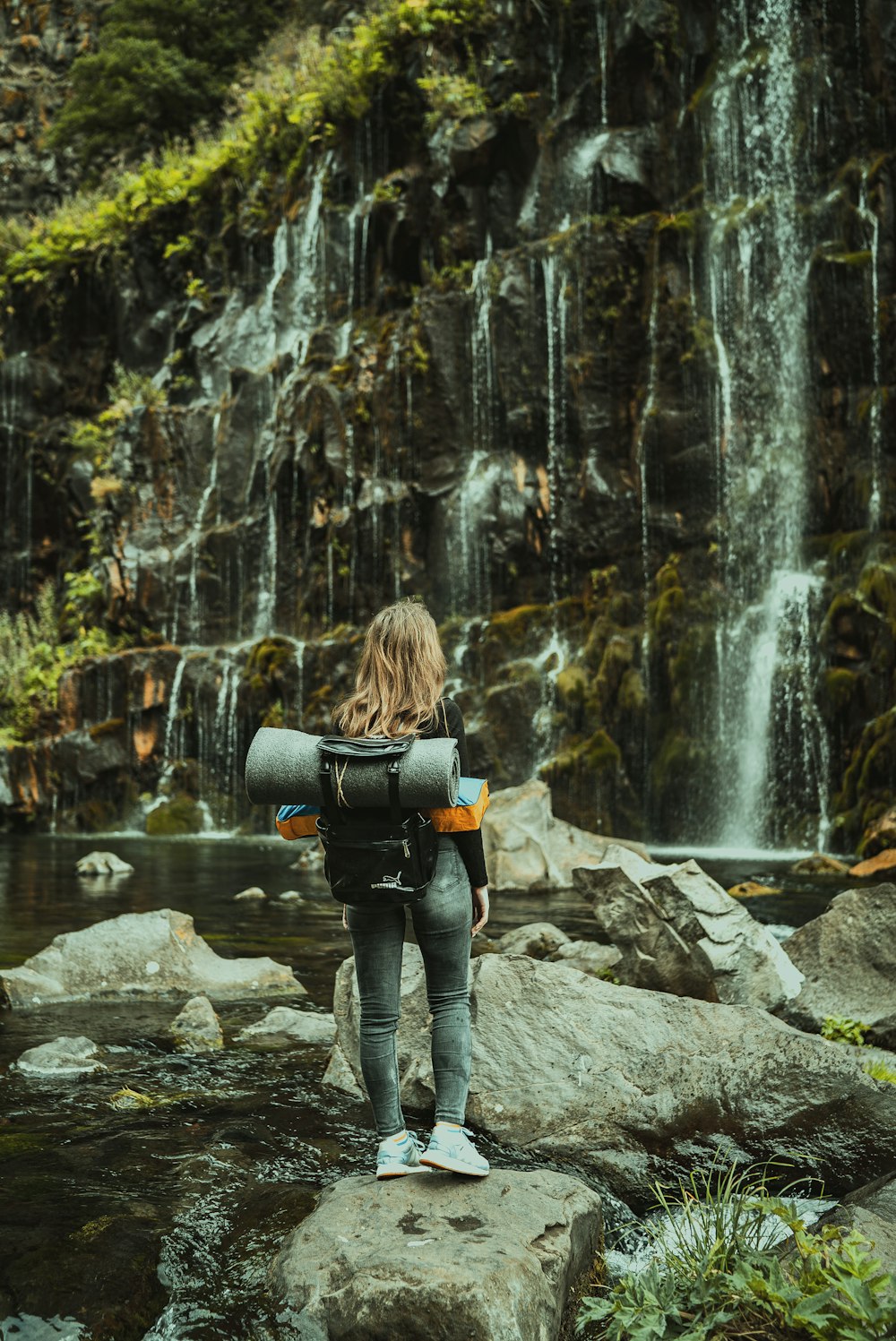 woman in black jacket and blue denim jeans holding black dslr camera standing on gray rock