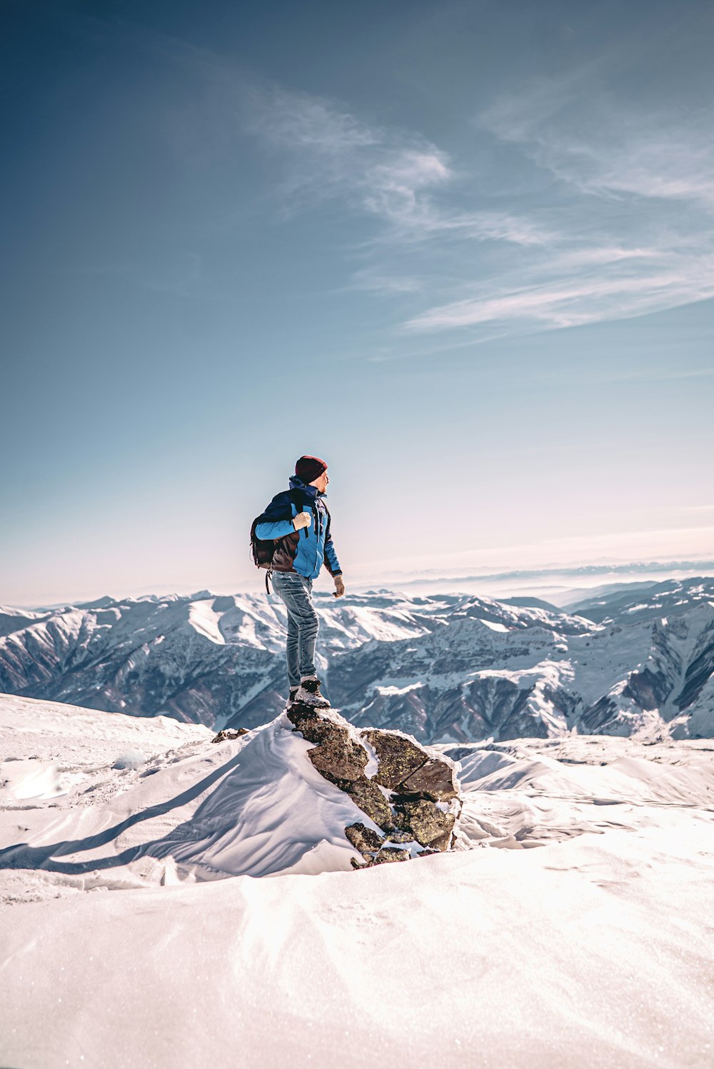 man in black jacket and blue denim jeans standing on snow covered mountain during daytime