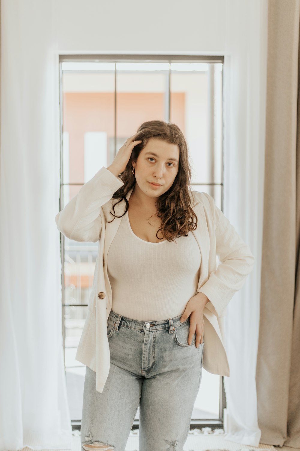 woman in white long sleeve shirt and blue denim jeans standing near window