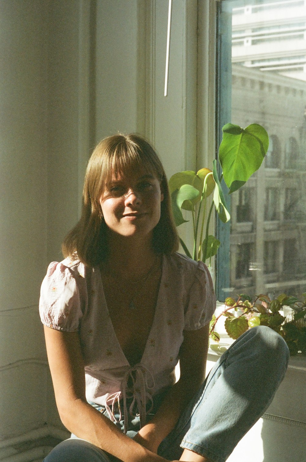 girl in pink button up shirt sitting beside green plant