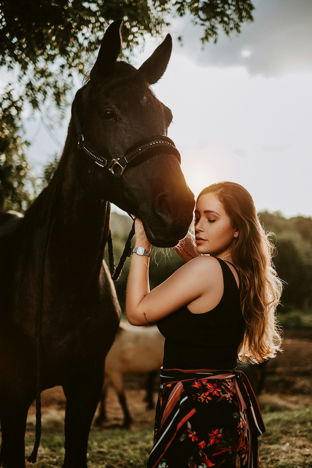 Mujer en camiseta sin mangas negra al lado del caballo marrón durante el día