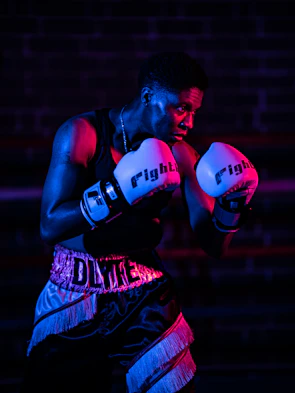 Close-up of a boxer’s focused face, sweat glistening under gym lights during an intense training session.