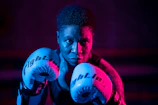 A close-up of a professional boxer’s gloved fists illuminated by electric blue neon lights.
