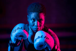 A close-up of a professional boxer’s gloved fists illuminated by electric blue neon lights.