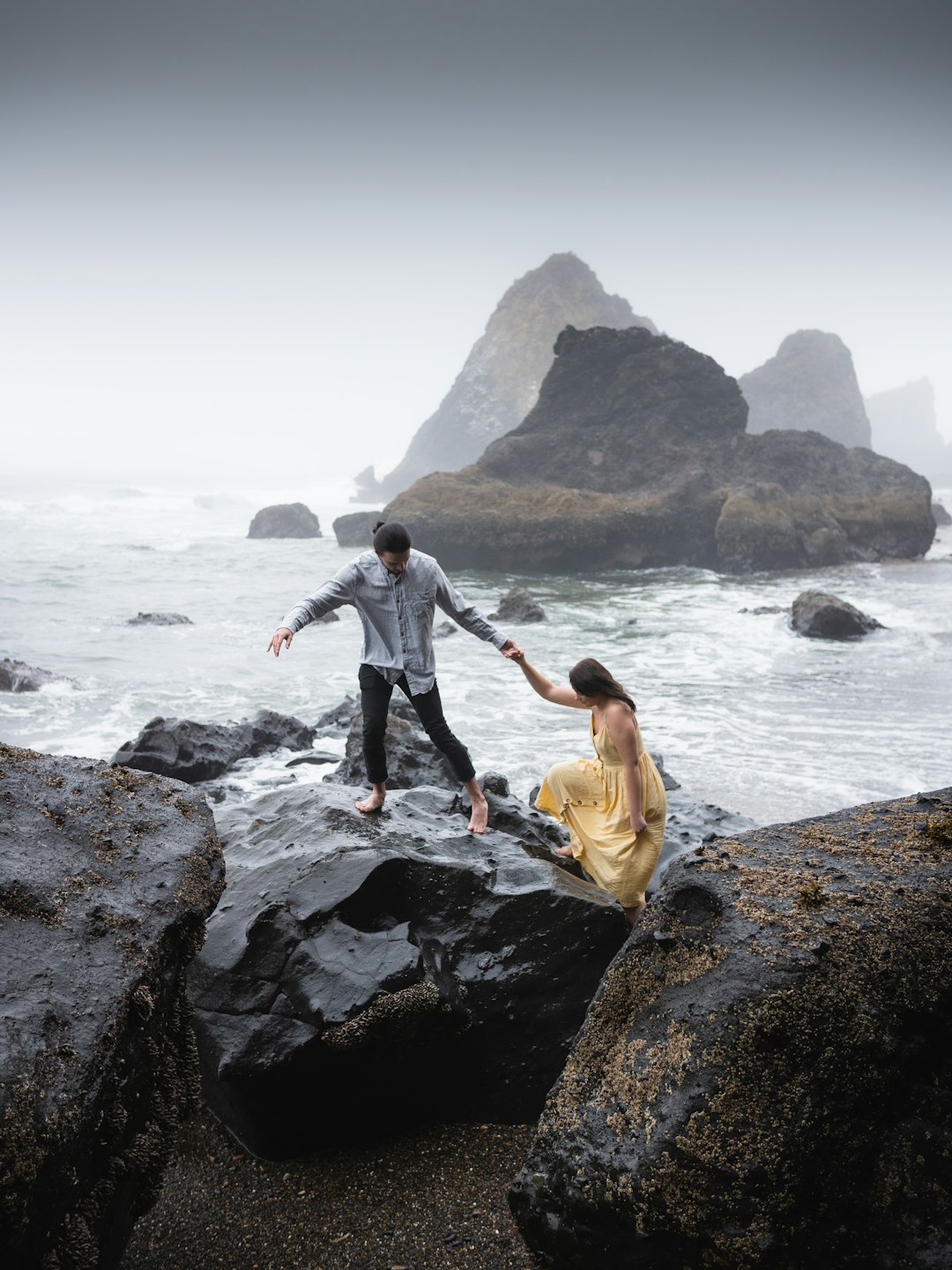 man and woman standing on rock near body of water during daytime