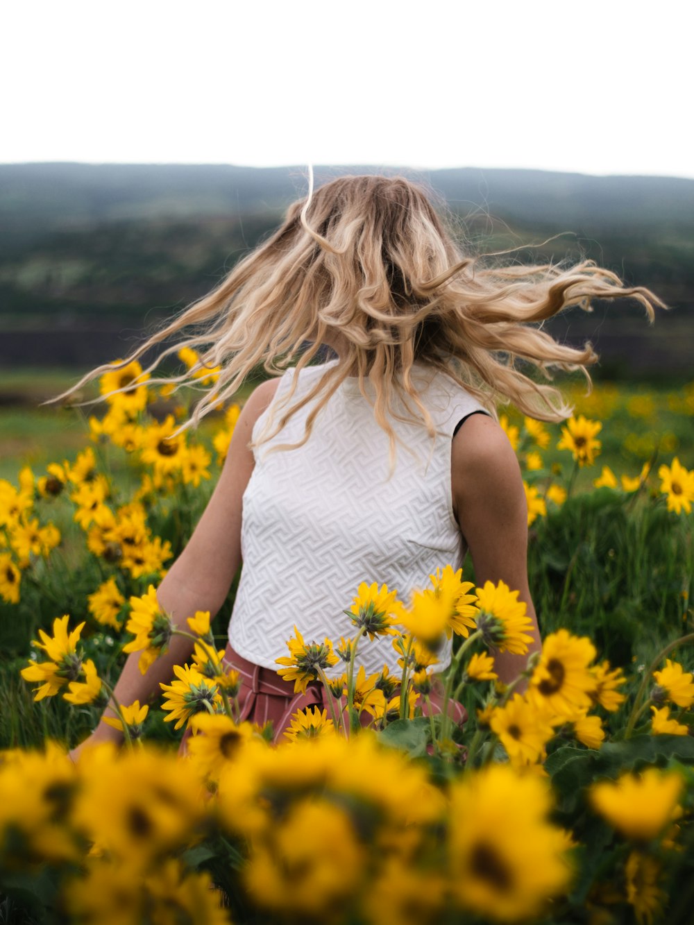 woman in white tank top standing on yellow flower field during daytime