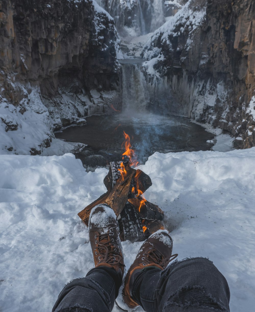 person in brown hiking shoes sitting on rock near bonfire during daytime