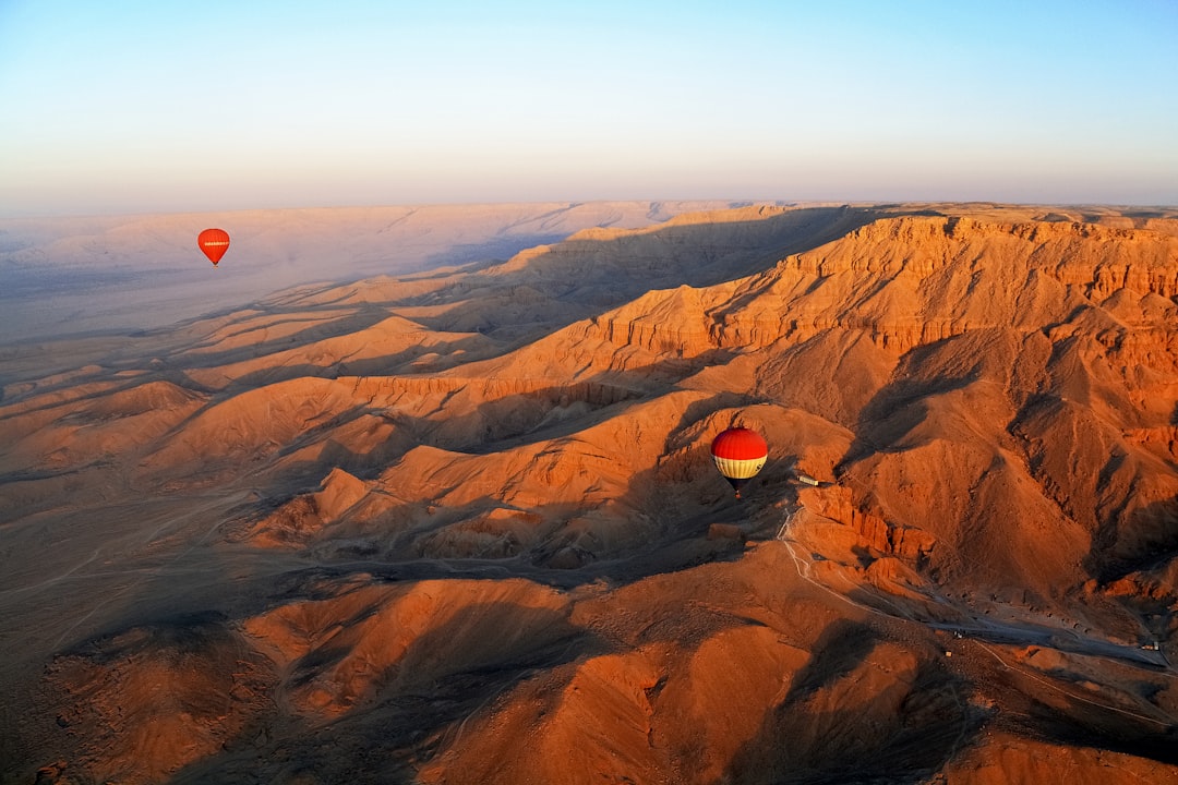 red hot air balloon flying over brown mountains during daytime