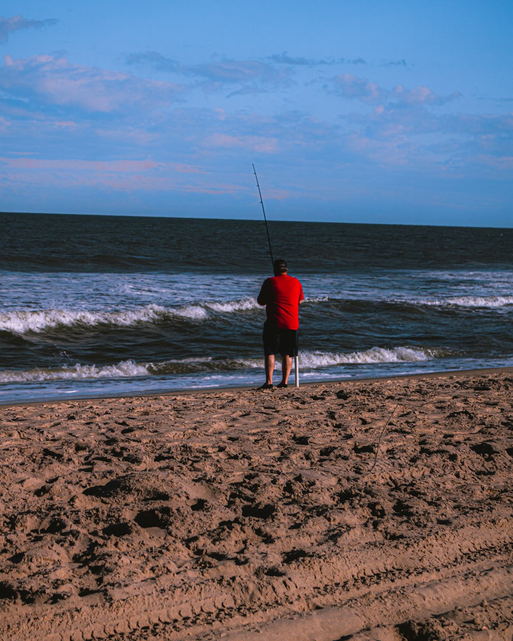 uomo in giacca nera e pantaloncini neri pesca sulla spiaggia durante il giorno