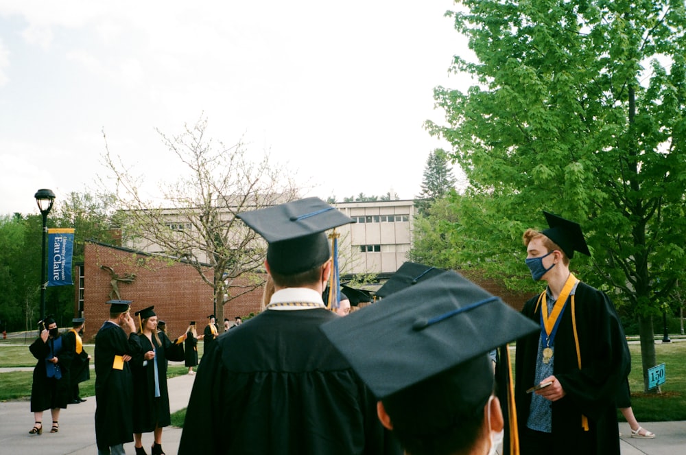 people in academic dress standing near green trees during daytime