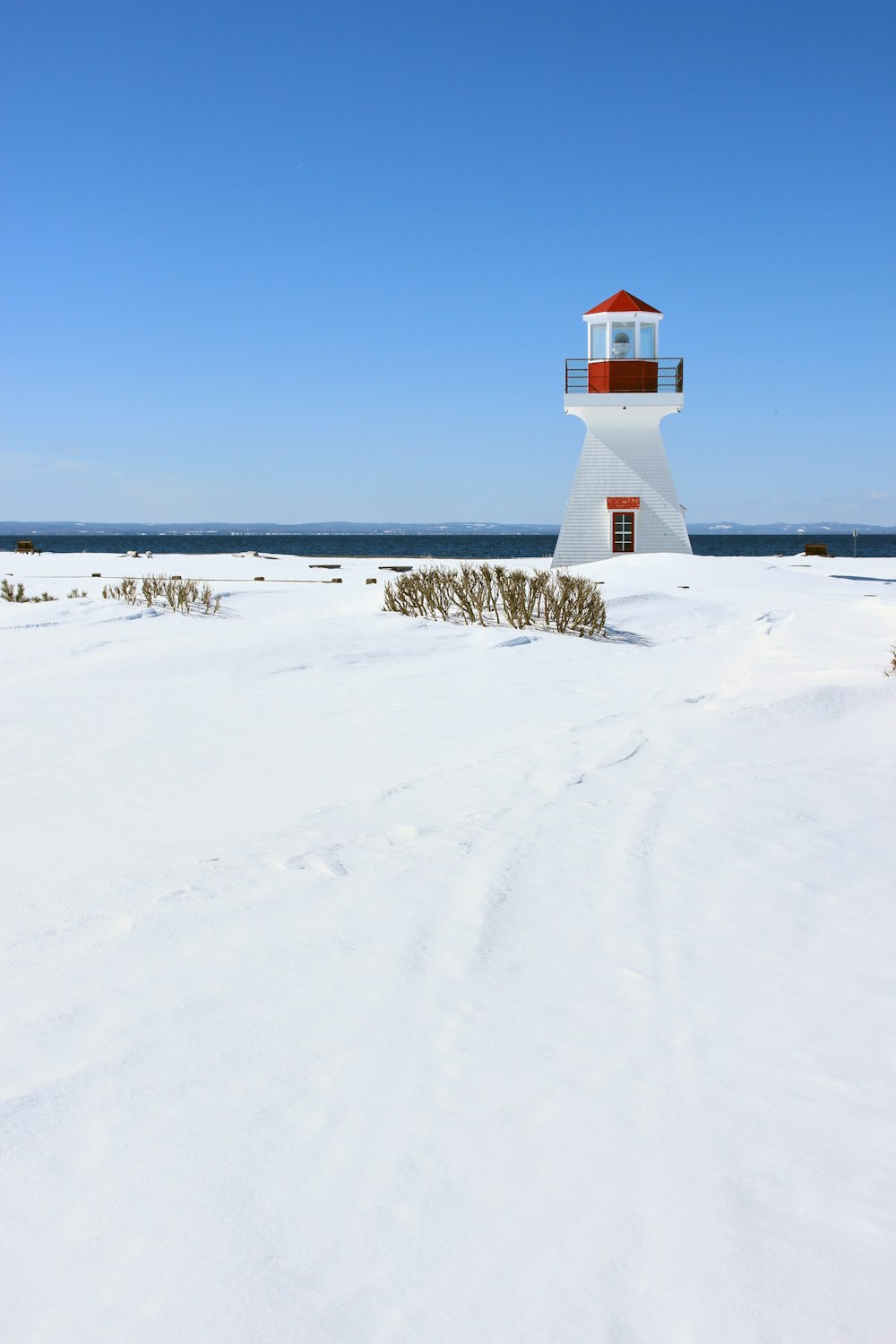 white and red lighthouse on snow covered ground under blue sky during daytime