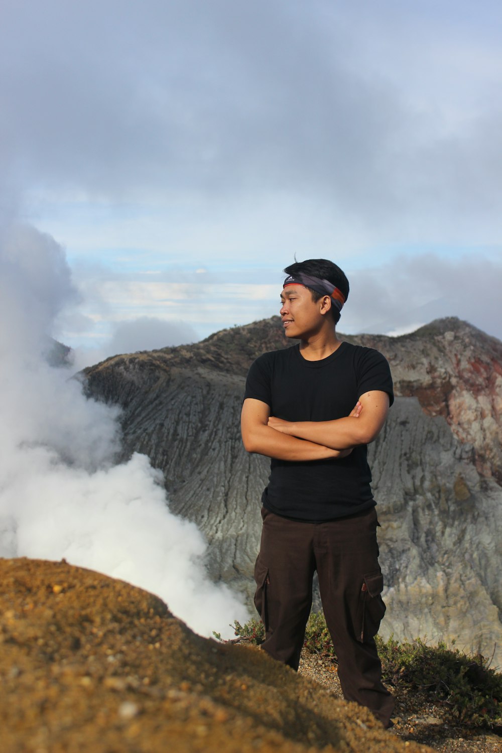 man in black crew neck t-shirt standing on brown rock formation under white clouds during