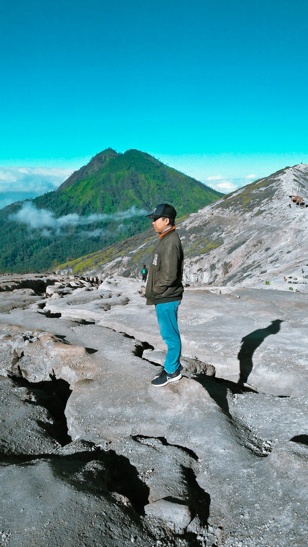 man in gray jacket standing on gray rock near green mountain during daytime