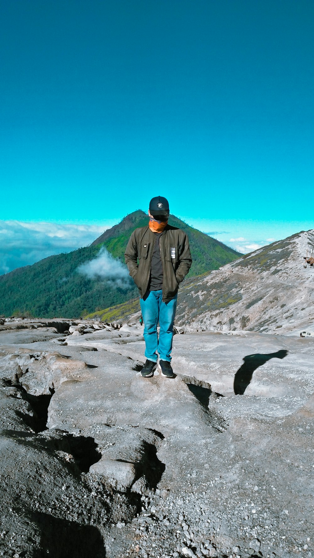 man in black jacket and blue denim jeans standing on rocky mountain during daytime
