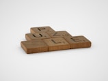 Wooden letter tiles spell out the word 'PUZZLE' on a flat surface. Each tile has a different letter with a small number in the corner, resembling Scrabble game pieces.