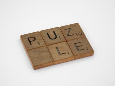Wooden tiles with letters and numbers resembling a Scrabble game, spelling the word 'PUZLE'.