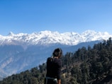 Scenic view of a woman in a black jacket on a green meadow with snowy Himalayan peaks in Dharamshala