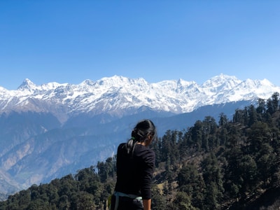 Scenic view of a woman in a black jacket on a green meadow with snowy Himalayan peaks in Dharamshala