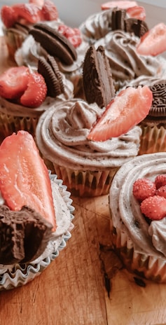 A close-up of colorful cupcakes topped with fresh berries and mint leaves on a rustic wooden table.