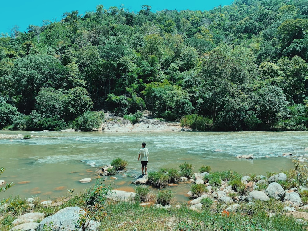 man in black shirt and black pants standing on brown rock near green trees during daytime