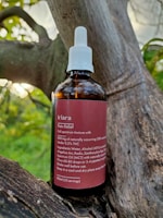 A brown glass bottle labeled 'kiara Pain Relief' is placed on a tree branch. The bottle has a white screw cap with a dropper. The label describes the contents as a full spectrum tincture, listing ingredients such as CBD and THC, along with usage instructions.
