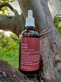 A brown glass bottle labeled 'kiara Pain Relief' is placed on a tree branch. The bottle has a white screw cap with a dropper. The label describes the contents as a full spectrum tincture, listing ingredients such as CBD and THC, along with usage instructions.