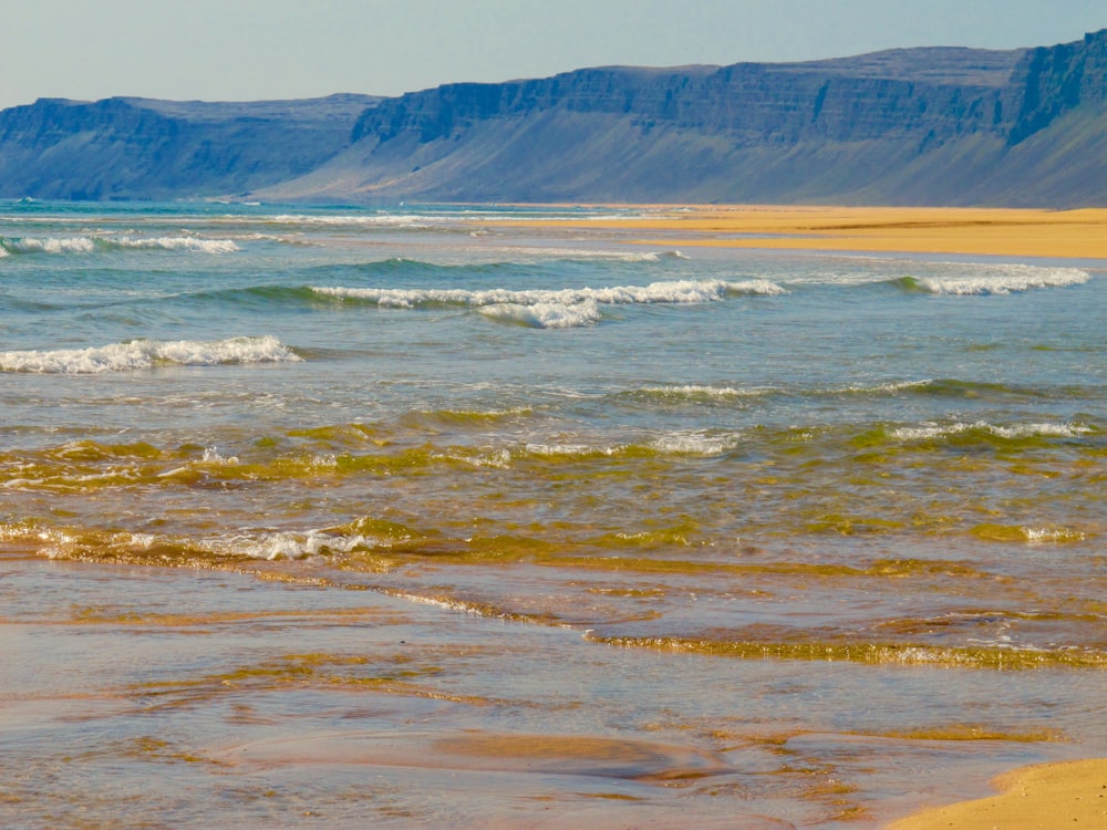 Montañas marrones y blancas cerca de una masa de agua durante el día