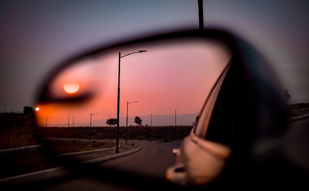 car side mirror showing road during sunset