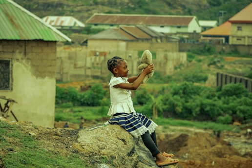woman in white shirt and blue and white plaid skirt sitting on brown rock during daytime