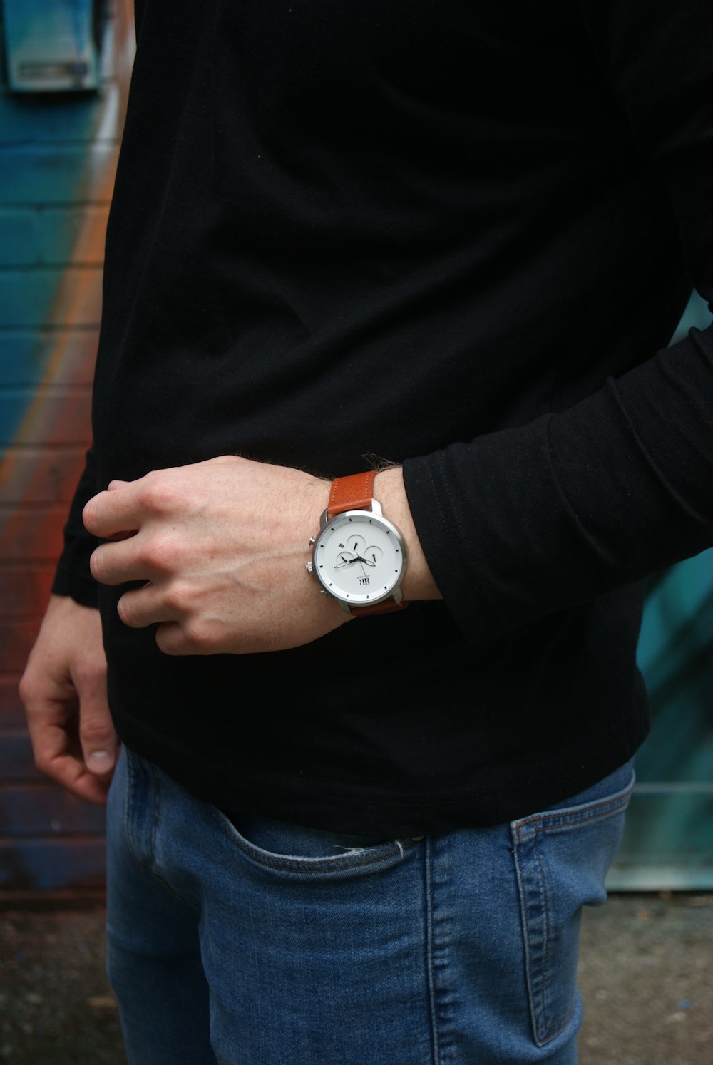 person in black long sleeve shirt and blue denim jeans wearing white analog watch