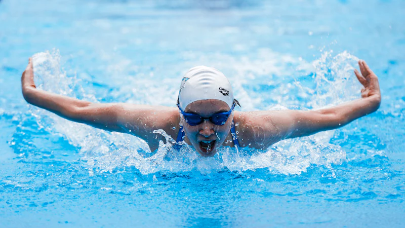 Swimmer in cap and goggles taking a breath during butterfly