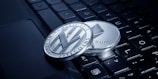 Two physical cryptocurrency coins, one Litecoin and one Ethereum, rest on the keys of a laptop keyboard. The coins display intricate engravings and are positioned at an angle that highlights their metallic sheen.