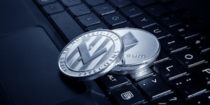 Two physical cryptocurrency coins, one Litecoin and one Ethereum, rest on the keys of a laptop keyboard. The coins display intricate engravings and are positioned at an angle that highlights their metallic sheen.