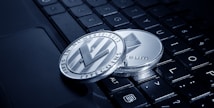 Two physical cryptocurrency coins, one Litecoin and one Ethereum, rest on the keys of a laptop keyboard. The coins display intricate engravings and are positioned at an angle that highlights their metallic sheen.