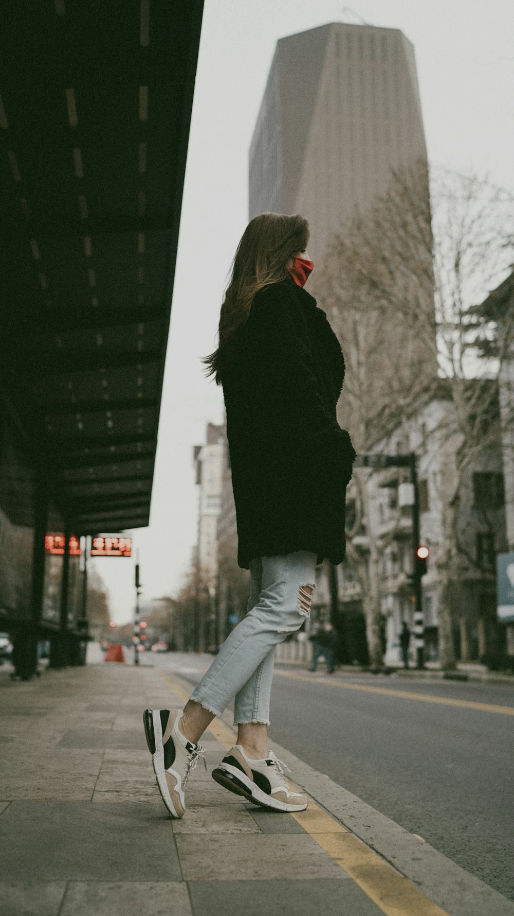 woman in black jacket and gray pants standing on sidewalk during daytime