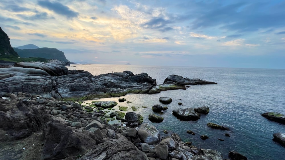 black rocks on sea shore under white clouds and blue sky during daytime