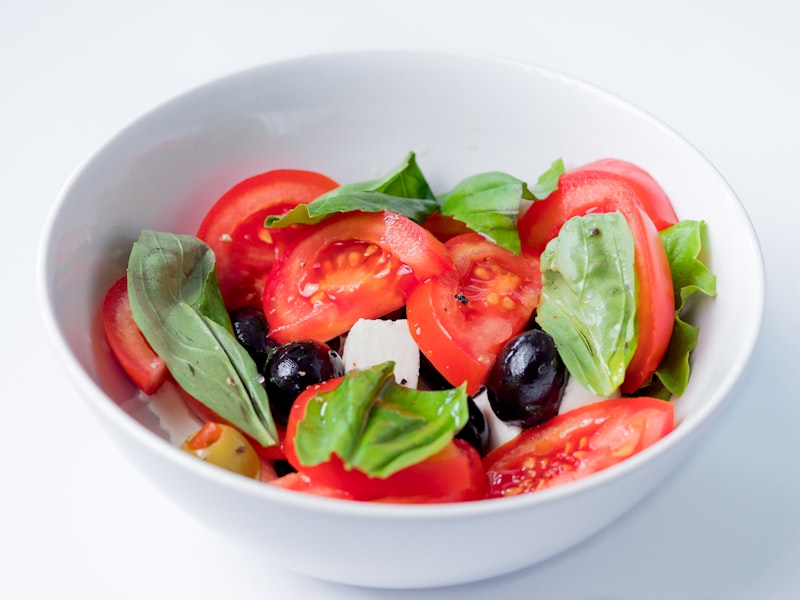 Close up photo of Italian Mediterranean Caprese salad with tomatoes, olives, mozzarella cheese, basil and olive oil dressing in a white bowl from unsplash}