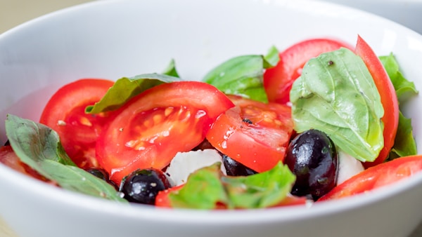 Sliced tomato and green leaf vegetable in white ceramic bowl