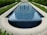 A long rectangular water feature with clear blue tiles, surrounded by trimmed green hedges and a paved stone pathway.