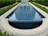 A long rectangular water feature with clear blue tiles, surrounded by trimmed green hedges and a paved stone pathway.