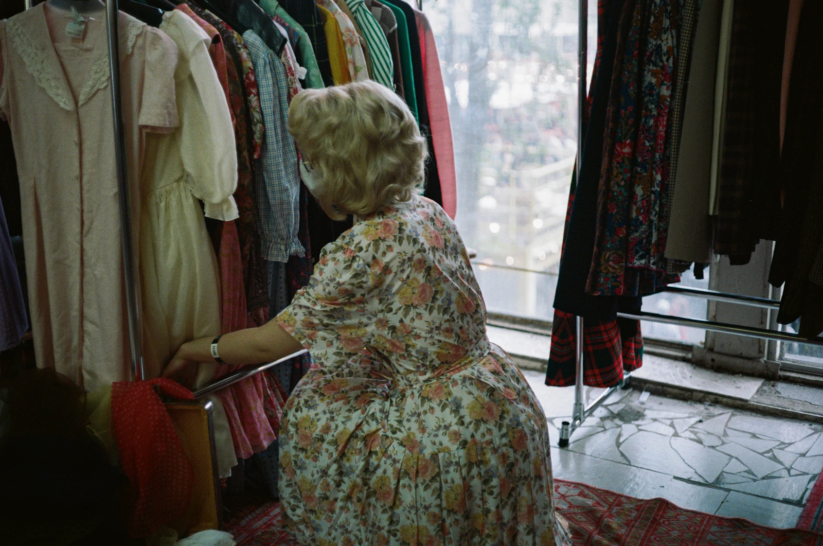 A woman in a floral dress browsing a rack of secondhand clothes.