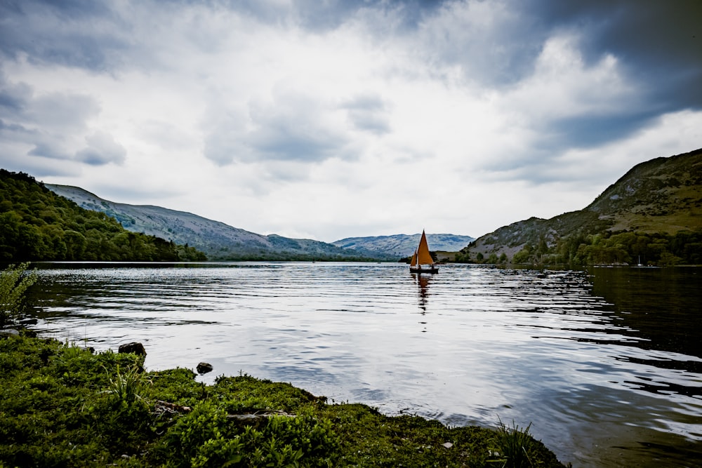 brown boat on lake near green grass field under white cloudy sky during daytime