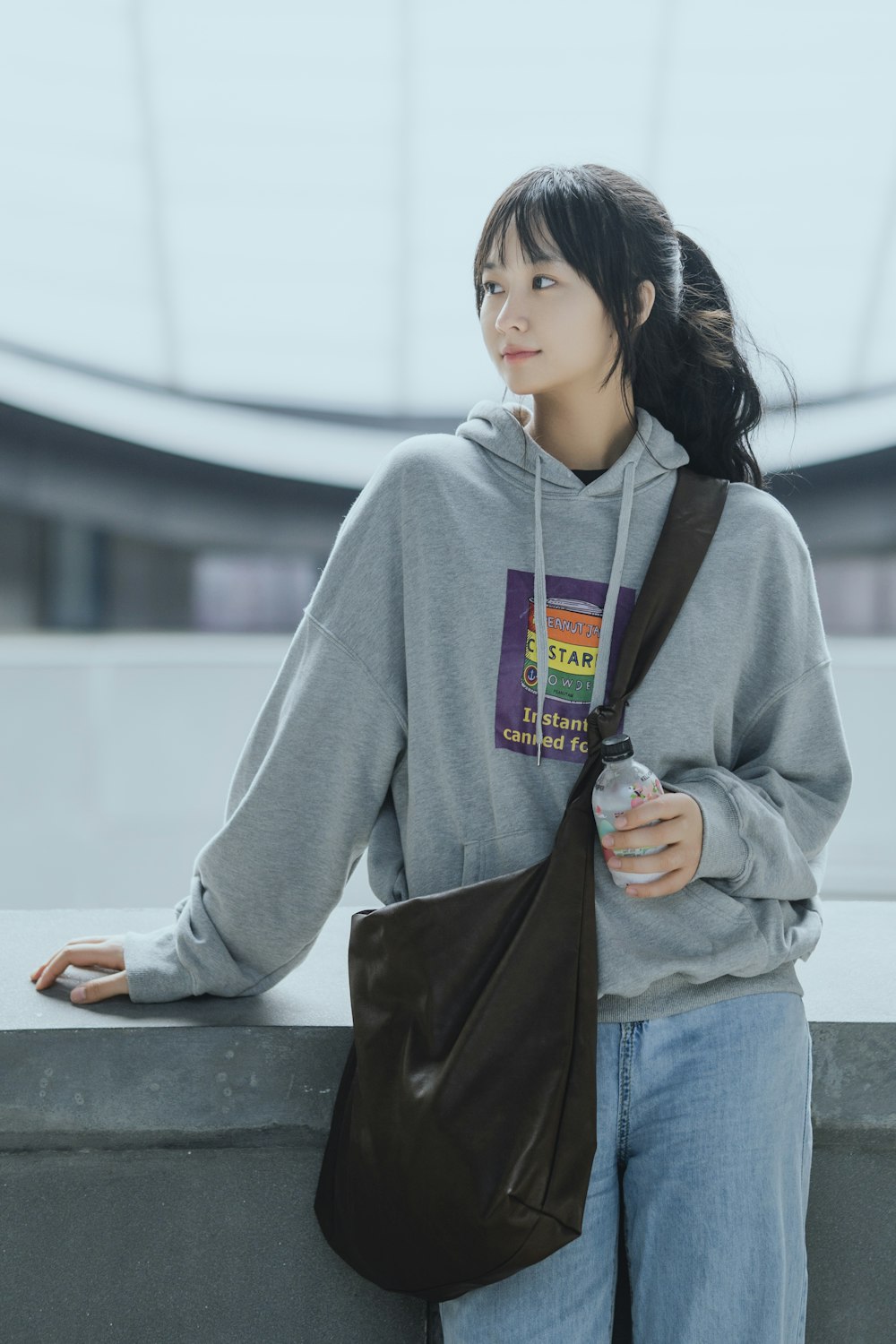 woman in gray hoodie holding black leather sling bag