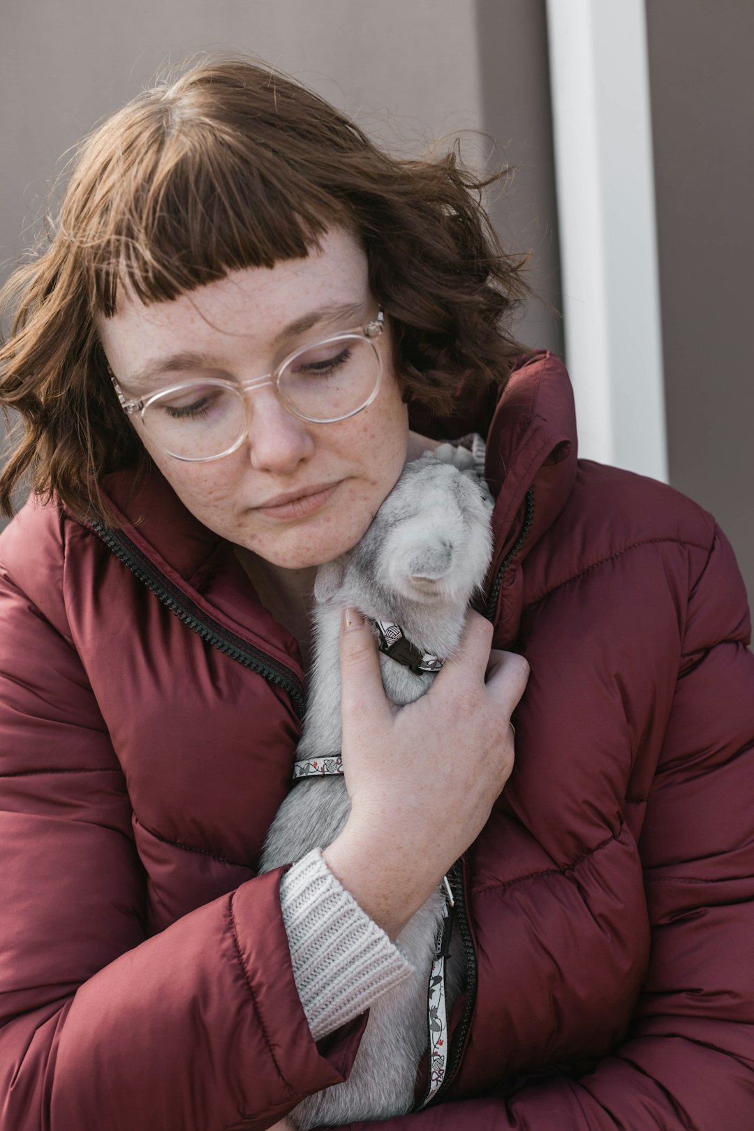 woman in red jacket holding gray puppy