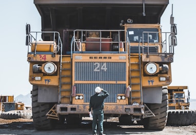 man in brown jacket standing beside yellow truck