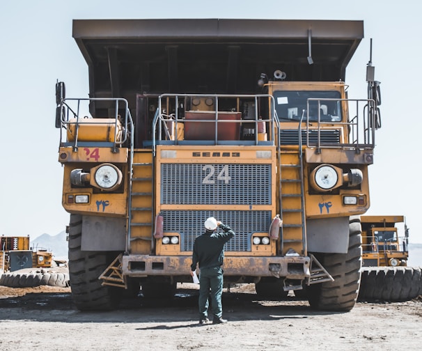 man in brown jacket standing beside yellow truck