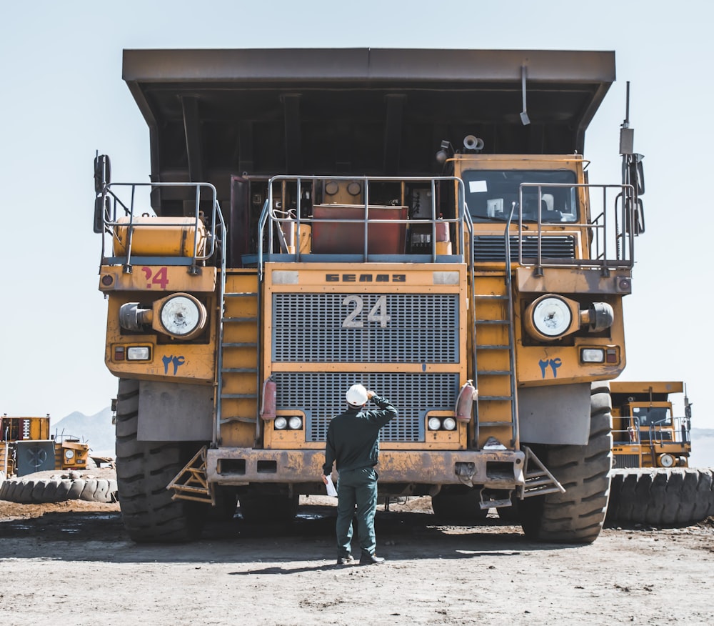 man in brown jacket standing beside yellow truck